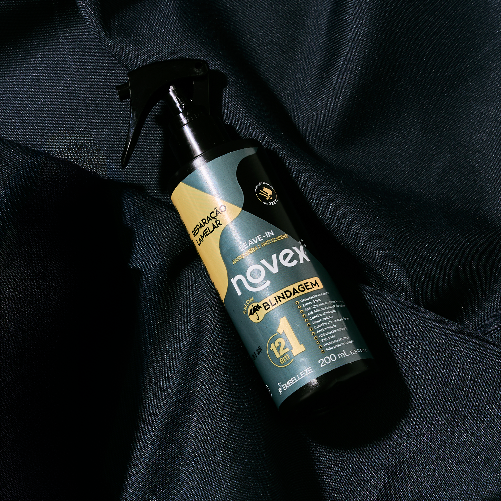 Leave-in Novex Salon Blindagem Reparação Lamelar da Embelleze de 200ml, com ação antiquebra e 12 em 1, em frasco spray preto deitado sobre um tecido escuro texturizado.